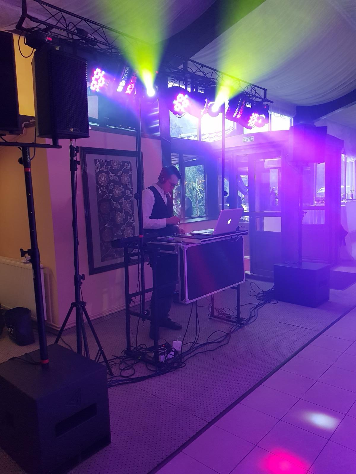DJ la consolă, cu lumini violet și verde într-o sală de evenimente